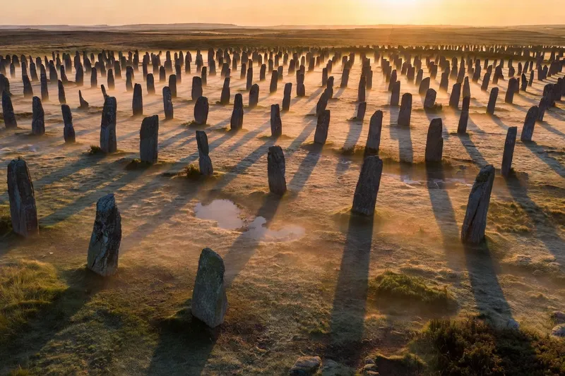 Alignements de Carnac au lever du soleil : files de menhirs en granit, ombres rasantes et brume basse sur la lande bretonne